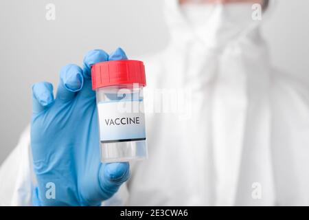 Flacon de vaccin Covid 19 dans la main des médecins. Médecin en combinaison de protection, masque facial, lunettes de sécurité et gants en caoutchouc démontrez le vaccin contre Banque D'Images