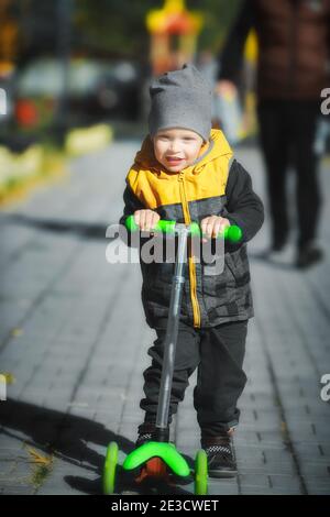 Un tout-petit heureux et émouvant prend un scooter à trois roues dans le parc le long du chemin. Banque D'Images