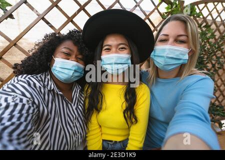 Amis multiraciaux portant un masque facial tout en prenant le selfie avec mobile Smartphone CAM pendant l'épidémie de virus corona - attention douce sur fille centrale Banque D'Images