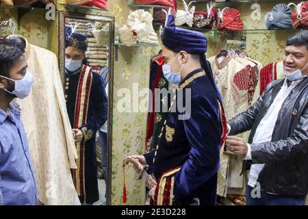 Dhaka, Bangladesh. 18 janvier 2021. Un vendeur a vu aider un marié à porter son costume et son turban dans un magasin avant sa cérémonie de mariage pendant la pandémie du coronavirus à Dhaka.de nombreux mariages ont été reportés en raison de la pandémie du coronavirus. Comme la situation pandémique au Bangladesh s'améliore de jour en jour, le programme social et culturel comme les cérémonies de mariage sont réorganisés de façon nouvelle et normale. Crédit : SOPA Images Limited/Alamy Live News Banque D'Images