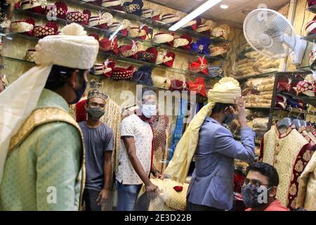 Dhaka, Bangladesh. 18 janvier 2021. Un vendeur a vu aider un marié à porter son costume et son turban dans un magasin avant sa cérémonie de mariage pendant la pandémie du coronavirus à Dhaka. De nombreux mariages ont été reportés en raison de la pandémie du coronavirus. Comme la situation pandémique au Bangladesh s'améliore de jour en jour, le programme social et culturel comme les cérémonies de mariage sont réorganisés de façon nouvelle et normale. Crédit : SOPA Images Limited/Alamy Live News Banque D'Images