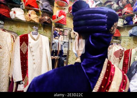 Dhaka, Bangladesh. 18 janvier 2021. Un marié portant un masque facial a vu sa combinaison et son turban se tester dans un magasin avant sa cérémonie de mariage pendant la pandémie du coronavirus à Dhaka.de nombreux mariages ont été reportés en raison de la pandémie du coronavirus. Comme la situation pandémique au Bangladesh s'améliore de jour en jour, le programme social et culturel comme les cérémonies de mariage sont réorganisés de façon nouvelle et normale. Crédit : SOPA Images Limited/Alamy Live News Banque D'Images