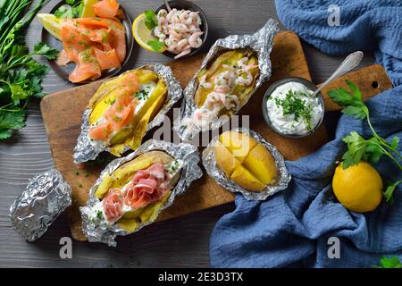 Divers types de pommes de terre cuites à la crème aigre aux herbes : nappées de saumon fumé, de jambon italien et de crevettes Banque D'Images