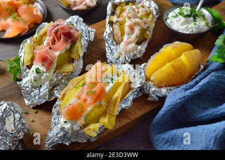 Divers types de pommes de terre cuites à la crème aigre aux herbes : nappées de saumon fumé, de jambon italien et de crevettes Banque D'Images