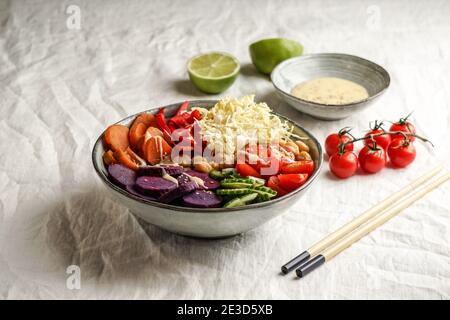 bol budha avec batata pourpre, poivrons, chou, patates douces, pois chiches, concombres sur la nappe blanche en lin Banque D'Images