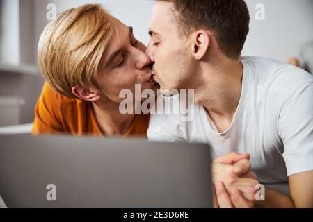 Un couple gay heureux s'embrasse et utilise un ordinateur portable à la maison Banque D'Images