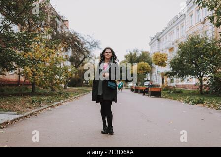 Jeune femme à poil long debout avec une tasse en papier de café sur l'allée et souriant Banque D'Images