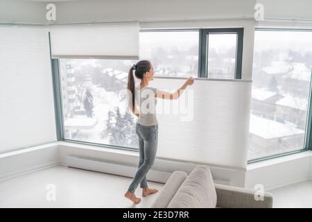 Femme ouvrant les rideaux de la maison dans l'appartement urbain. Moderne haut en bas en haut intimité nuances cellulaires sur la fenêtre de l'appartement de garder la chaleur en hiver avec Banque D'Images