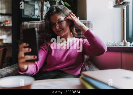 À la taille de la bonne dame assise à la table café tout en faisant le selfie sur son smartphone Banque D'Images