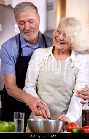 un couple de personnes âgées prépare une salade de légumes dans la cuisine, un homme aux cheveux gris aide sa femme à cuisiner, à prendre un petit déjeuner sain. concentrez-vous sur les mains Banque D'Images