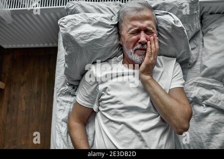 triste sénior sénichée au lit dans un hôpital, concept d'hospitalisation. souffrant de maladie, douleurs dentaires, pleurs de douleur Banque D'Images