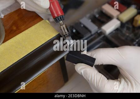 restauration de surfaces en bois, maître avec un fer à souder et de la cire pour combler un défaut sur le mobilier de près Banque D'Images