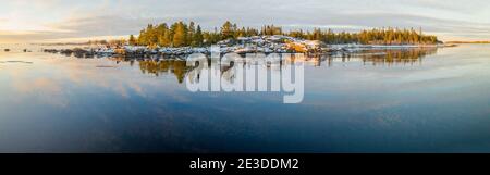 Vue panoramique sur le coucher de soleil d'hiver réflexions de la mer Iced à la petite péninsule rocailleuse de Kont, Umea, Suède. Hiver forêt de pins scandinaves à Banque D'Images