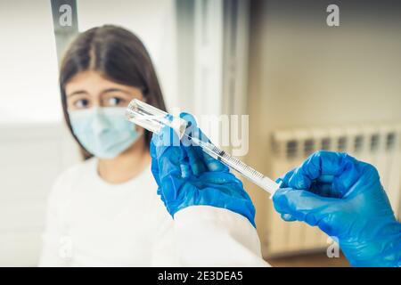 Infirmière administrant le vaccin du coronavirus à une jeune fille patiente avec masque facial à la clinique du médecin. Immunisation, traitement médical et Covid-19 v Banque D'Images