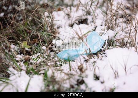 Un masque médical débasable utilisé est jeté comme des détritus sur le sol enneigé du parc forestier. Déchets de coronavirus. Déchets polluants Banque D'Images