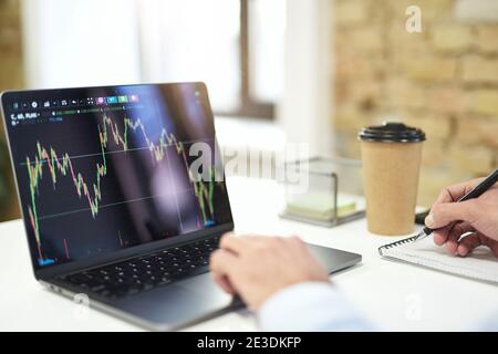 Gros plan d'un ordinateur portable moderne au bureau et une personne qui exploite les données et prend des notes Banque D'Images