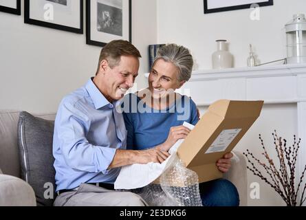 Bon vieux couple senior déballage livraison boîte de livraison assis à la maison sur le canapé. Banque D'Images