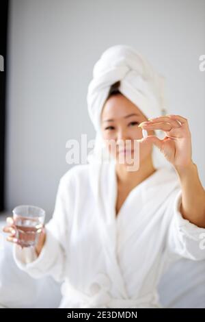 femme sur le point de prendre un comprimé, tenant des pilules dans les mains, se concentrer sur des pilules. jeune femme attrayante assise sur le lit à la maison et prenant des analgésiques avec de l'eau. Banque D'Images