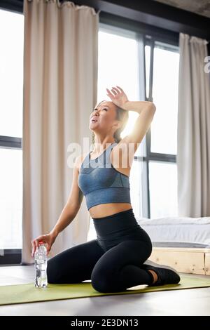 fit femme assis essuyant la transpiration de son visage, se reposer, fatigué après des exercices durs, entraînement à la maison Banque D'Images