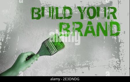 Construisez vos mots de marque sur le mur gris avec le pinceau dans la main. Concept de marketing d'entreprise motivationnel. Banque D'Images