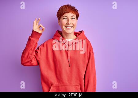 bonne redhead femme montre ok geste, tout sera ok, sourire. isolé Banque D'Images