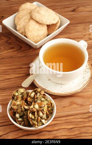 Biscuits aux amandes et biscuits aux graines de citrouille enrobées de sucre dans un saladier et une tasse de thé vert sur une table en bois. Gros plan Banque D'Images