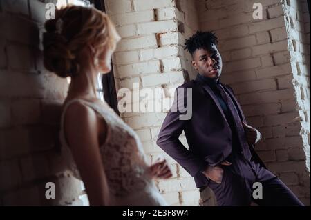 Chic et à la mode, le marié afro-américain se tient devant la mariée caucasienne posant. Banque D'Images