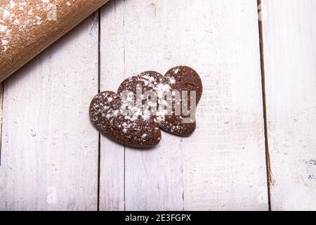 Biscuits au chocolat pour la période la plus douce de l'année. Deux biscuits, l'un à côté de l'autre, avec de la farine et un rollpin sur une table en bois sabée. Banque D'Images