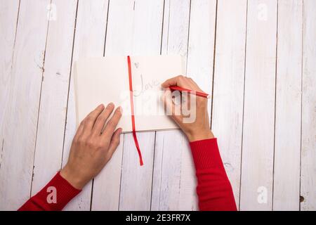 Des mains de femmes écrivant un joli message sur son ordinateur portable. La touche rouge du pull et du crayon rappelle la couleur de la Saint-Valentin. Fond en bois blanc Banque D'Images