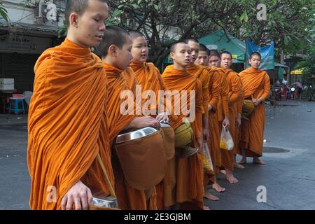 Les moines bouddhistes débutants avec leurs alms bols sur leur traditionnel matin alms ronde (Binta Baat), s'arrêtant pour dire une prière; Bangkok, Thaïlande Banque D'Images