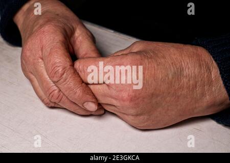 Les mains pliées de la femme âgée reposent sur la table. Rides sur les mains. Solitude des personnes âgées. Banque D'Images