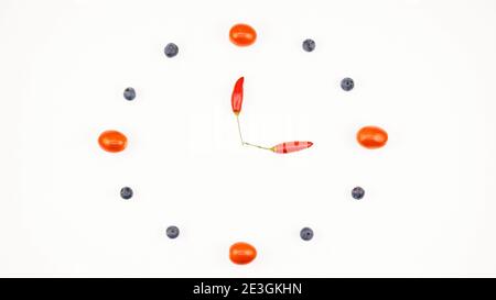 Une horloge de tomates cerises, de bleuets et de piments rouges sur fond blanc montrant l'heure. Espace pour le texte. Banque D'Images