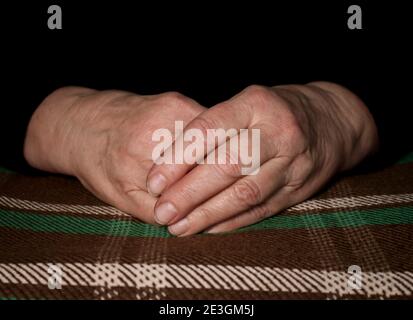 Les mains de la vieille femme claquées reposent sur un tissu à carreaux. Rides sur les mains. Solitude des personnes âgées. Soins infirmiers et soins aux parents âgés. Banque D'Images
