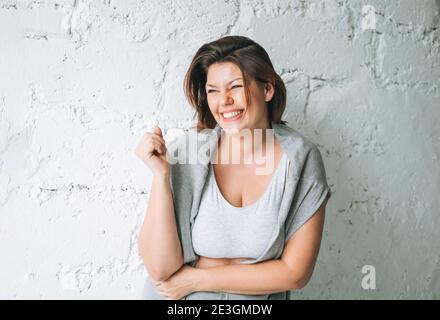Belle heureuse affective brunette jeune femme plus taille corps positif dans le sport confortable porter près du mur de brique blanche Banque D'Images