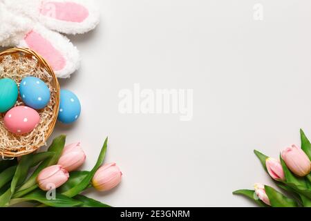 Joyeuses Pâques. Oeufs multicolores dans un panier, tulipes, branche de coton sur fond gris. Espace de copie de carte de vœux à plat. Banque D'Images