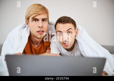 Couple gay mignon utilisant un ordinateur portable moderne à la maison Banque D'Images