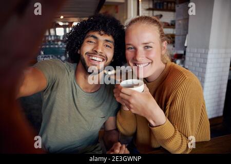 Portrait d'un homme souriant avec une petite amie tenant une tasse de café selfie dans un café moderne Banque D'Images