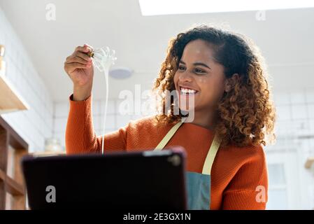 Bonne jeune femme afro-américaine ayant des appels vidéo avec une tablette ordinateur tout en cuisinant dans la cuisine à la maison Banque D'Images