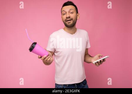 Photo d'un jeune homme de brunette non rasé et confiant avec barbe porter un t-shirt rose clair de tous les jours isolé sur fond rose tenant et Banque D'Images