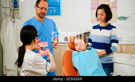 Médecin montrant à l'enfant l'hygiène dentaire correcte à l'aide d'une maquette de squelette de dents. Dentiste tenant un échantillon de mâchoire humaine avec une brosse à dents dans un bureau de stomatologie travaillant avec un assistant d'homme. Banque D'Images