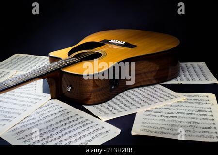 feuilles avec partitions musicales et guitare acoustique classique jaune à six cordes avec un pickguard noir sur un arrière-plan noir isolé Banque D'Images