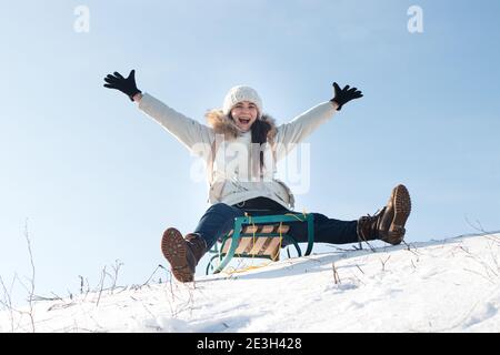 En hiver, la femme s'assoit et se couche de neige sur fond de neige et de ciel. Fille rit et se réjouit dans la neige, divertissement dans le traîneau Banque D'Images