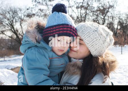 Maman et son fils se câlinent en hiver sur fond de nature et de neige. Paysage d'hiver et amour de maman, Fête des mères. Des vacances actives dans la nature Banque D'Images