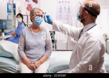 Médecin prenant la température de la patiente senior comme prévention pendant le coronavirus. Personnel médical en clinique effectuant un examen pour les infections, les maladies et le diagnostic. Banque D'Images