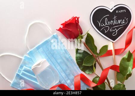 Contexte conceptuel de la célébration de la Saint Valentin avec affiche avec texte bonne Saint Valentin et rose avec masques et gel hydroalcoolique. Vue de dessus. Banque D'Images