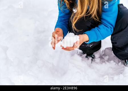 Fille blonde jouant dans la neige faisant une boule de neige avec ses mains et portant un chandail bleu Banque D'Images