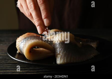 La femelle salante à la main le poisson de hareng dans une assiette noire sur bois arrière-plan Banque D'Images