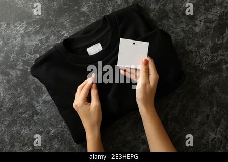 Les mains des femmes tiennent le sweat-shirt et l'étiquette vierge sur la table noire Banque D'Images