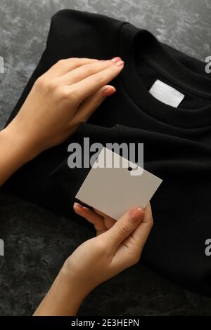 Les mains des femmes tiennent le sweat-shirt et l'étiquette vierge sur la table noire Banque D'Images