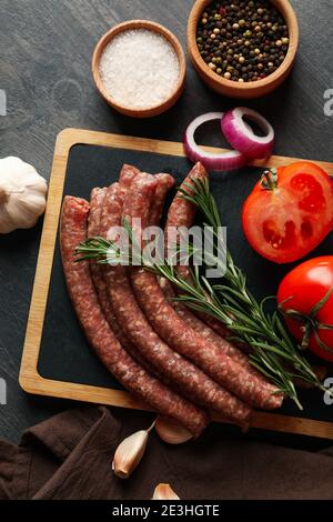 Embarquez avec des saucisses crues, des herbes et des épices sur fond sombre Banque D'Images